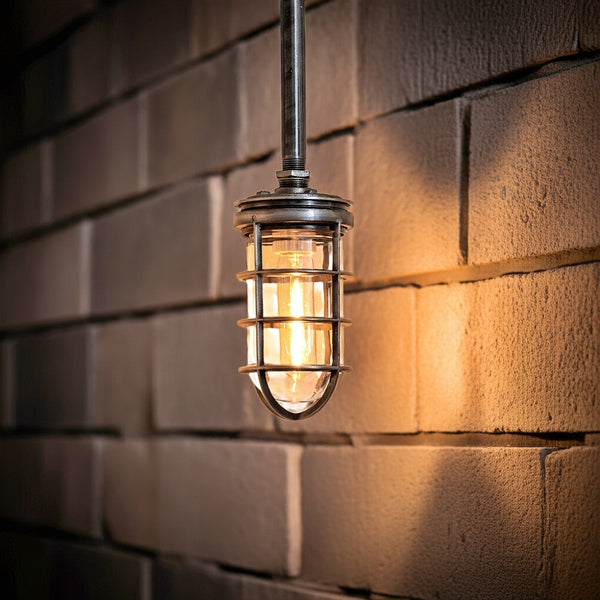 A vintage-style industrial light fixture with a metal cage and exposed bulb hanging against a textured brick wall, casting a warm glow.