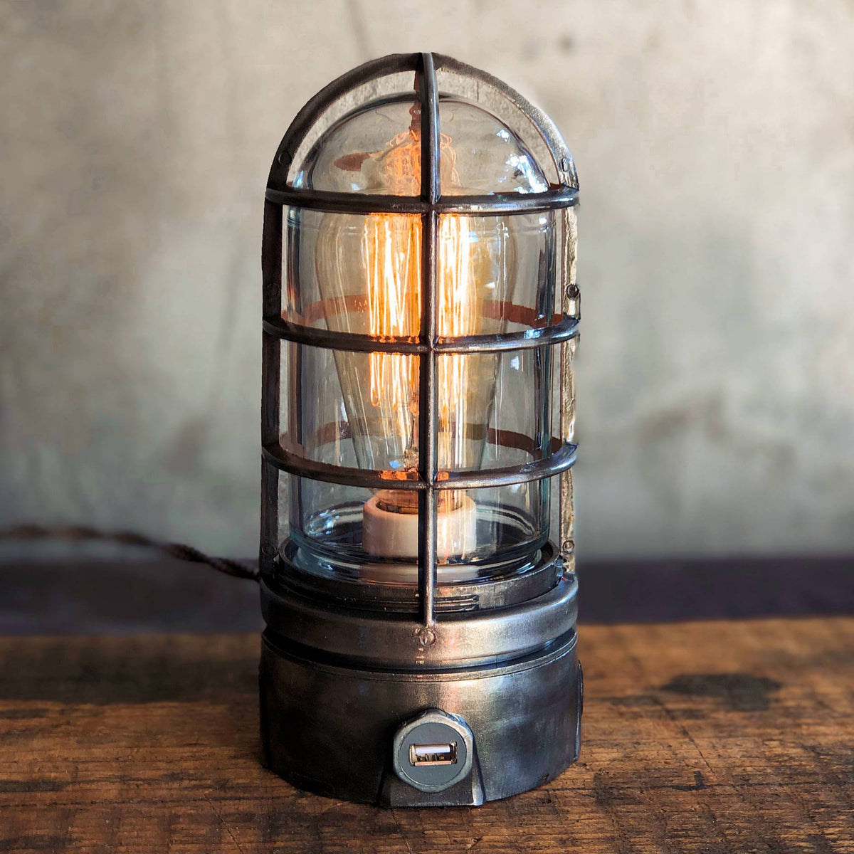 Dark gray metal cage industrial table lamp with a built in usb port on rustic wood table