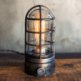 Dark gray metal cage industrial table lamp with a built in usb port on rustic wood table