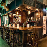 Five MillerLights 'The Beacon' industrial caged ceiling lights installed under a wooden overhead canopy illuminating a rustic craft beer brewery taproom and pub bar counter.