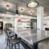 A row of MillerLights 'The Beacon' industrial caged ceiling lights integrated into an exposed electrical conduit network across a modern raw concrete ceiling in an open-concept office building.