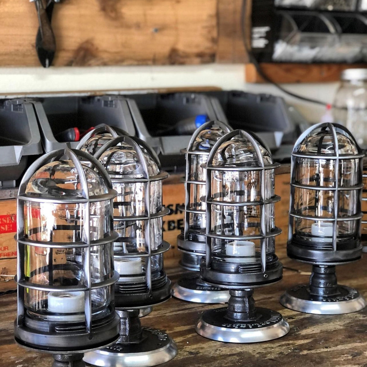 A row of handcrafted 'The Beacon' industrial semi flush mount ceiling lights sitting on a wooden workbench during small-batch production at the MillerLights workshop in Huntington Beach, California.