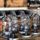 A row of handcrafted 'The Beacon' industrial semi flush mount ceiling lights sitting on a wooden workbench during small-batch production at the MillerLights workshop in Huntington Beach, California.