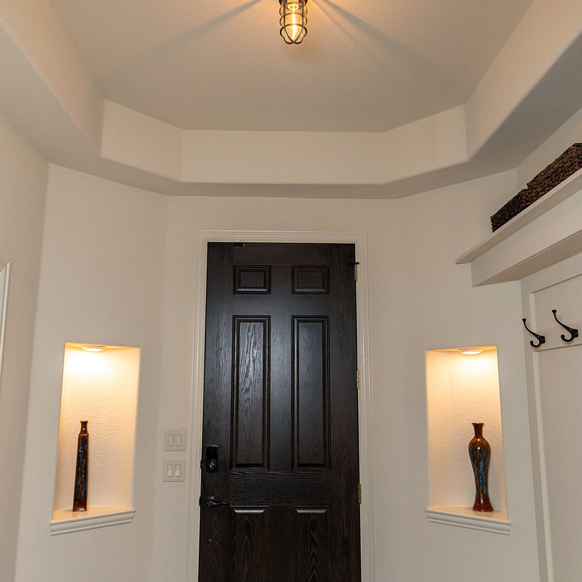 MillerLights 'The Beacon' industrial semi flush mount cage ceiling light installed in a residential home foyer entryway, casting an x-shaped ambient shadow pattern above a dark wood front door.