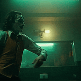 Cinematic shot from the Joker 2019 movie bathroom dance scene featuring Arthur Fleck, with the MillerLights industrial double cage vanity light fixture mounted centrally above the mirror.