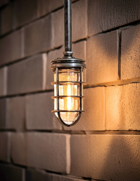A vintage-style industrial light fixture with a metal cage and exposed bulb hanging against a textured brick wall, casting a warm glow.