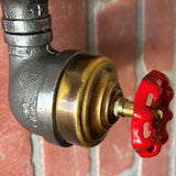 Close-up of a hand turning the red metal faucet knob on a steampunk rotary light switch.