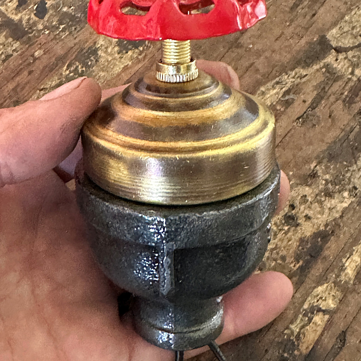  Close-up of a handcrafted steampunk lamp switch featuring a vibrant red industrial faucet handle on aged iron pipe fittings.
