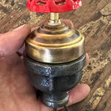  Close-up of a handcrafted steampunk lamp switch featuring a vibrant red industrial faucet handle on aged iron pipe fittings.