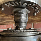 Close-up view of MillerLights 'The Beacon' industrial ceiling light mount, showcasing the cast iron canopy with stamped brand name, antiqued steel hex nuts, and heavy-duty iron pipe coupling joints.