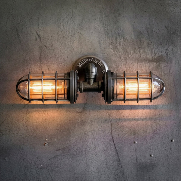 MillerLights industrial double cage wall sconce illuminated with a warm orange glow from vintage Edison bulbs, mounted on a textured gray concrete wall.